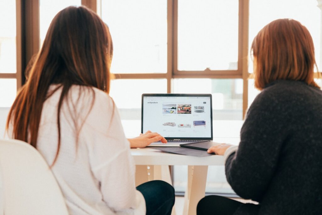 Two women collaborate at a table with a laptop, discussing integrated software solutions for better client engagement